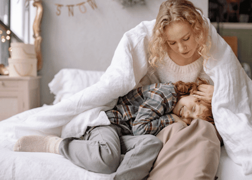 A woman and child snuggled together under blankets on a cozy bed, sharing warmth and comfort.