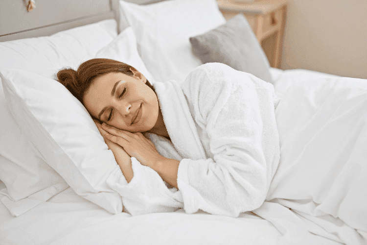 Woman sleeping peacefully on a white bed wearing a soft bathrobe.