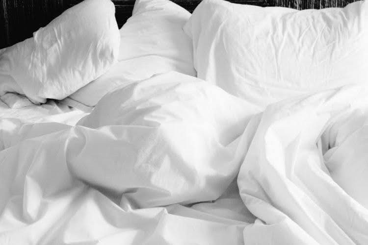 White bed sheets and pillows left rumpled and unmade after sleep.
