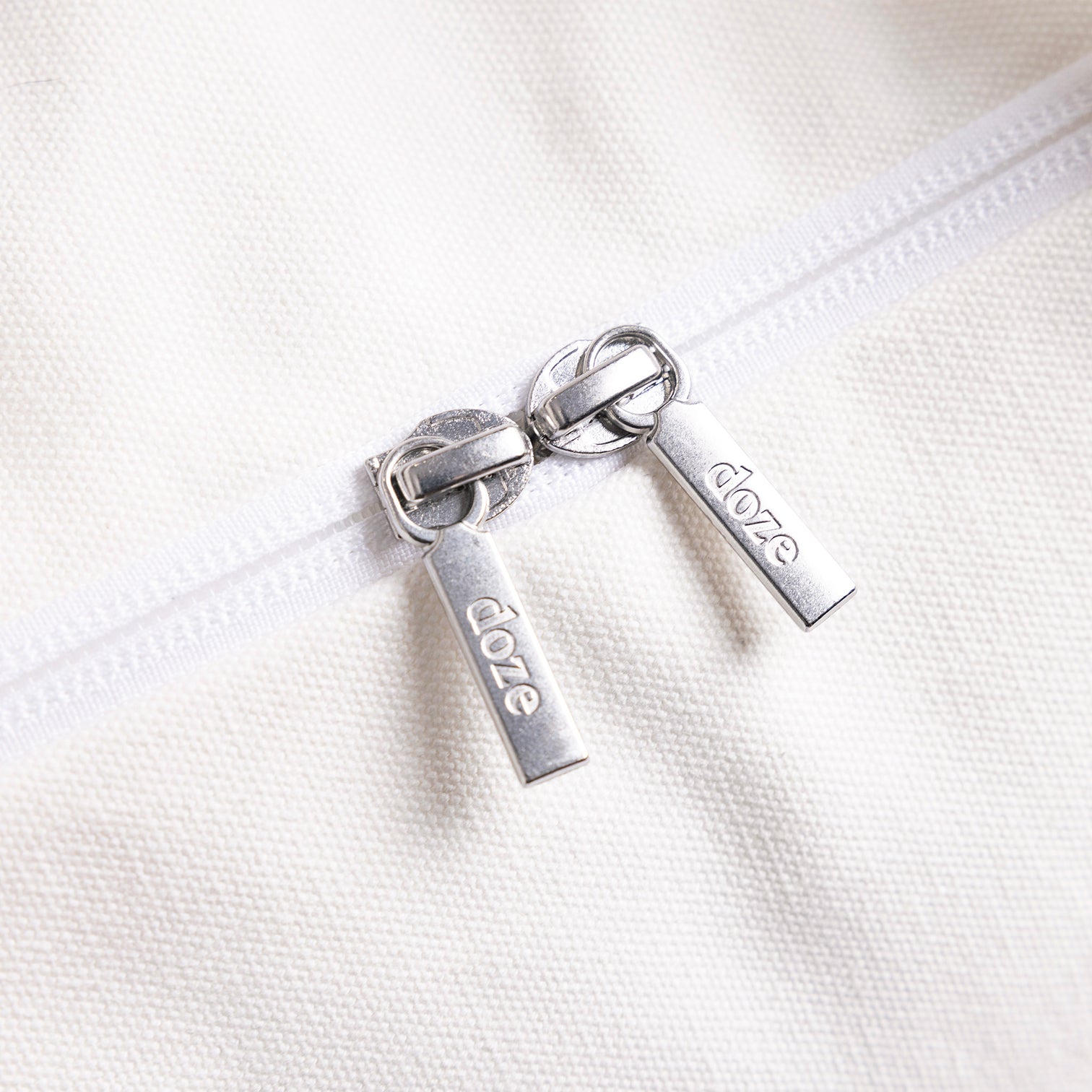 Close-up of two silver zipper pulls on white fabric.